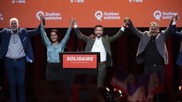 Des élus de Québec solidaire lèvent les bras en l'air en se tenant par la main, sur scène.