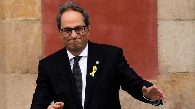 M. Torra, qui porte un ruban jaune, sourit tout en levant les mains.