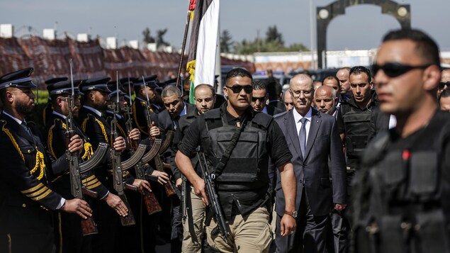 Un homme lourdement armé précède le premier ministre Hamdallah lorsqu'il passe devant une haie d'honneur formée de policiers du Hamas. Un homme lourdement armé précède le premier ministre Hamdallah lorsqu'il passe devant une haie d'honneur formée de policiers du Hamas.