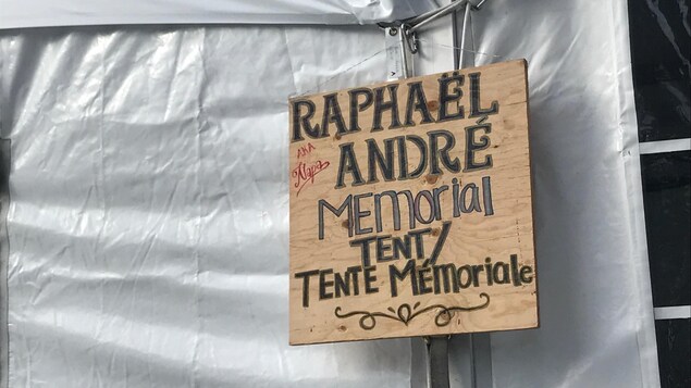 Un panneau en bois sur lequel on peut lire : ''Raphaël André (aka Napa) Memorial Tent/Tente Mémoriale''.