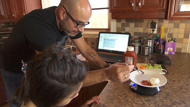 Giada Raposo observe attentivement son père qui prépare le repas de sa petite sœur Tiana. Il y a du ketchup sans sucre et de la mayonnaise dans l'assiette qui se trouve sur la balance. Giada Raposo observe attentivement son père qui prépare le repas de sa petite sœur Tiana. Il y a du ketchup sans sucre et de la mayonnaise dans l'assiette qui se trouve sur la balance.