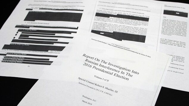 Quatre pages du rapport Mueller, dont la page titre, sont étalées sur une table. On peut voir des sections caviardées.