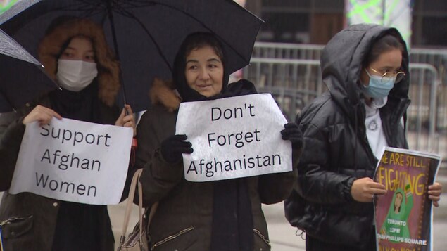 ثلاث نساء مرتديات معاطف سوداء يحملن أوراقاً طُبعت عليها دعوات مثل ’’ادعموا نساء أفغانستان‘‘ و’’لا تنسوا أفغانستان‘‘. 