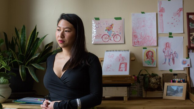 À sa table de travail, l'artiste montréalaise Ravy Puth pose devant ses illustrations accrochées au mur.