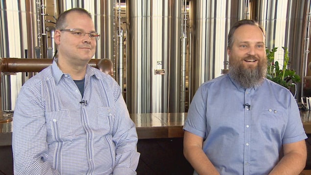 Ray Muzyka et Greg Zeschuk sont assis devant des cuves de bières en inox.