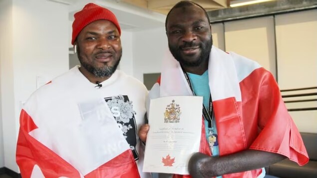 Razak Iyal, left, and Seidu Mohammed are draped in Canadian flags after they officially became citizens earlier this month. The two friends almost lost their lives as they walked across the U.S. border in the freezing cold to get to Canada, back in 2016. (Ian Froese/CBC)