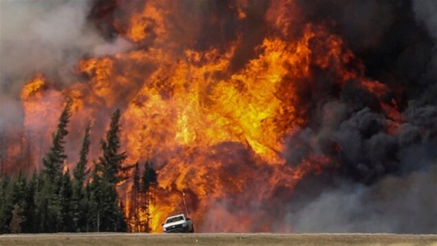 Image d'une camionnette devant un énorme feu de forêt dans les environs de Fort McMurray, en Alberta, en 2016.