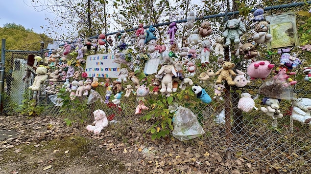 Des peluches sur un grillage entourent le panneau où il est inscrit "Elle a joué ici mais n'est jamais rentrée à la maison".