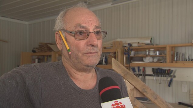Un homme donne une entrevue à Radio-Canada dans un établi alors que des outils se retrouvent en arrière-plan. Un homme donne une entrevue à Radio-Canada dans un établi alors que des outils se retrouvent en arrière-plan.