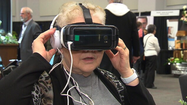 Une dame porte un casque de réalité virtuelle sur la tête, avec des écouteurs.