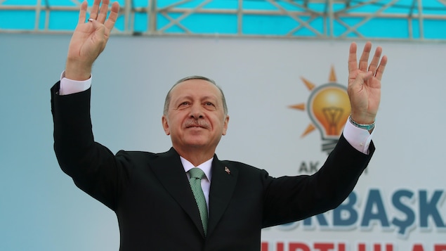 Le président Erdogan, les deux bras dans les airs, sur une scène. Le président Erdogan, les deux bras dans les airs, sur une scène.