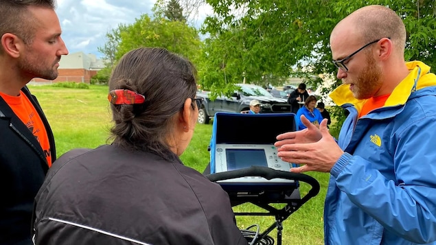 Un homme explique à deux personnes comment les recherches par radar près d'un ancien pensionnat pour Autochtones en Saskatchewan. 