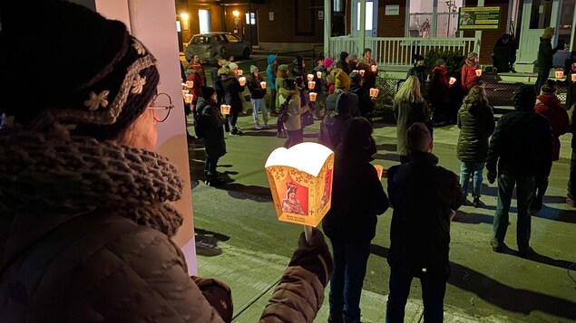 Des personnes portant un flambeau sont debout, devant la galerie les bureaux du Comité de solidarité/Trois-Rivières. 