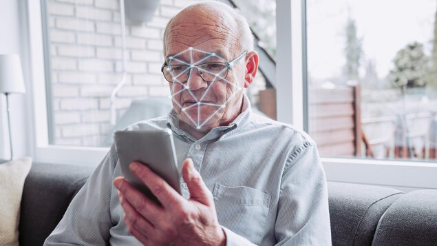 Un logiciel de reconnaissance faciale scanne le visage d'un homme âgé qui tient un téléphone intelligent.