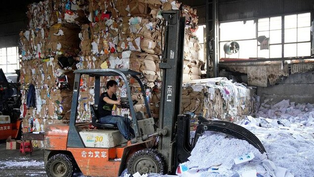 Un véhicule conduit par un ouvrier pousse une quantité importante de papier délaissé sur le sol d'une usine.
