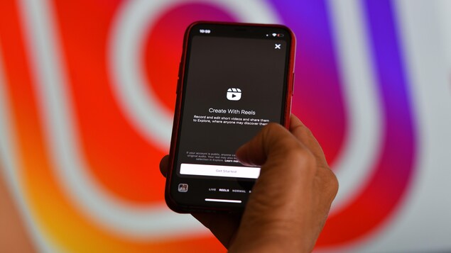Un téléphone intelligent affiche la fonctionnalité Reels, devant un logo géant d'Instagram. 