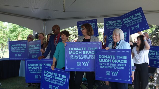 Un groupe de personnes brandissant des pancartes sur lesquelles on peut lire «Donate this much space».