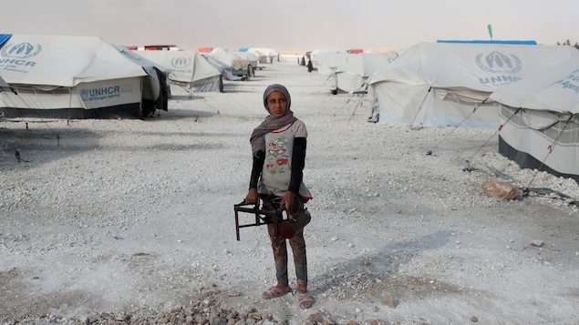 Une adolescente tient un brûleur pour faire la cuisine en plein milieu d'un camp de déplacés à Raqqa, en Syrie. Des tentes l'entourent. Une adolescente tient un brûleur pour faire la cuisine en plein milieu d'un camp de déplacés à Raqqa, en Syrie. Des tentes l'entourent.