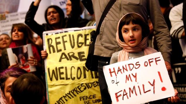 Une petite fille tient une affiche sur laquelle est écrit : « Ne touchez pas à ma famille! » Une petite fille tient une affiche sur laquelle est écrit : « Ne touchez pas à ma famille! »