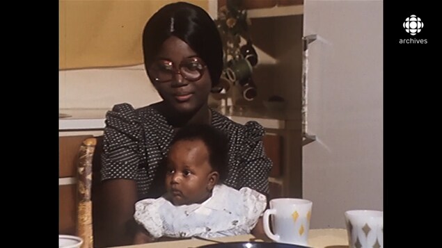 Femme haïtienne assise à la table d'une cuisine avec sa fille de 4 mois sur les genoux..