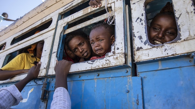 Plusieurs enfants regardent par les fenêtres sans vitre d'un autobus vétuste. Le plus jeune est en pleurs.