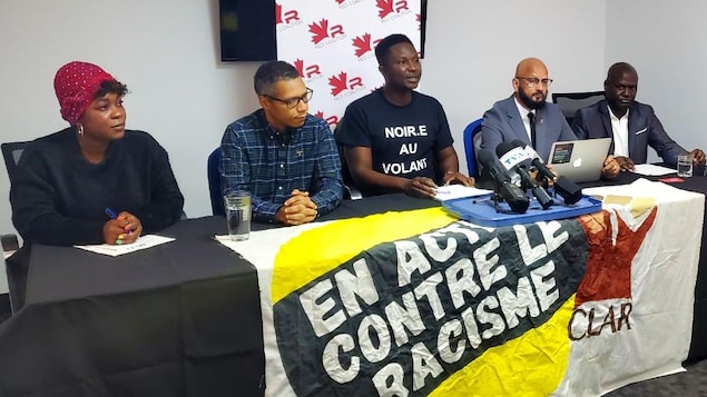 5 représentants de groupes anti-racisme derrière une table et un micro en conférence de presse.