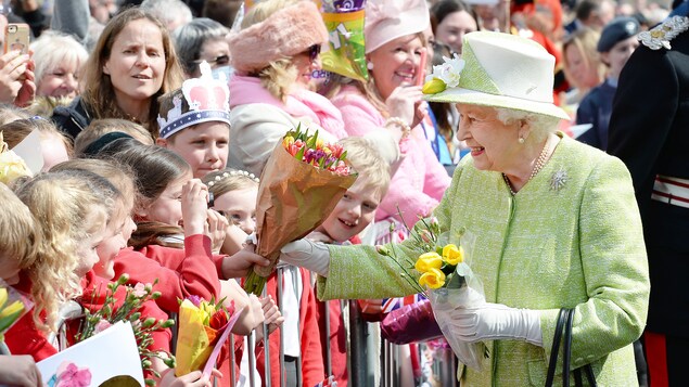La reine reçoit un bouquet de fleurs des mains d'une fillette La reine reçoit un bouquet de fleurs des mains d'une fillette