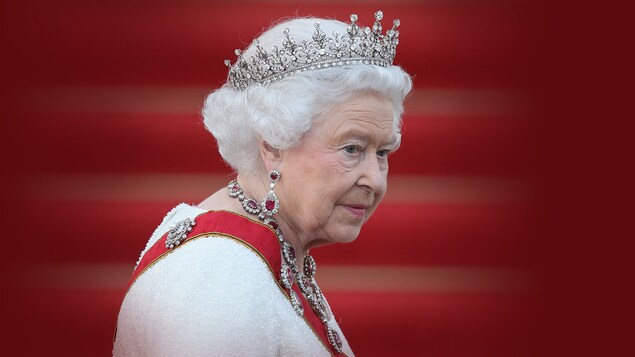 Une photo d'Élisabeth II devant un fond rouge. Elle porte des bijoux, dont une couronne.