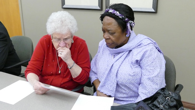 Deux femmes assises regardent atttentivement une feuille de papier. Deux femmes assises regardent atttentivement une feuille de papier.