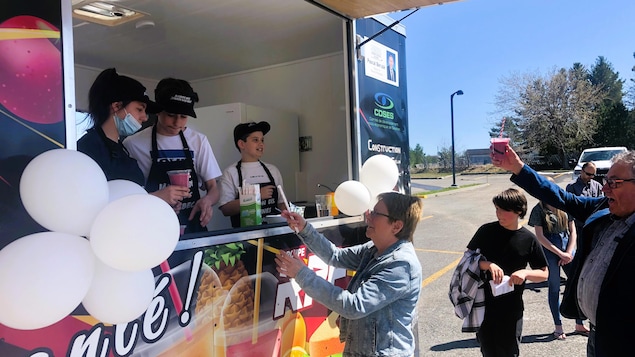 Des jeunes dans une remorque de style food-truck servant de la nourriture à des clients. 