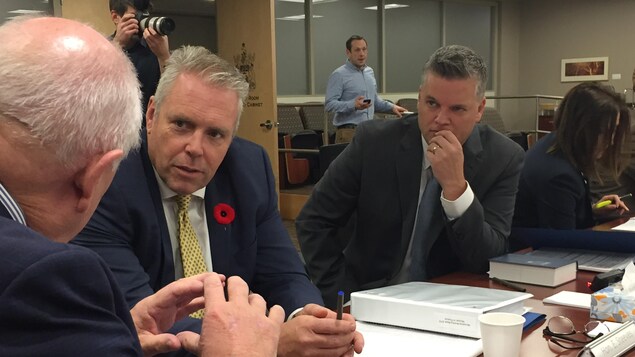Ernie Steeves et Robert Gauvin assis à la table discutent. Il y a de nombreux dossiers devant eux. Ernie Steeves et Robert Gauvin assis à la table discutent. Il y a de nombreux dossiers devant eux.