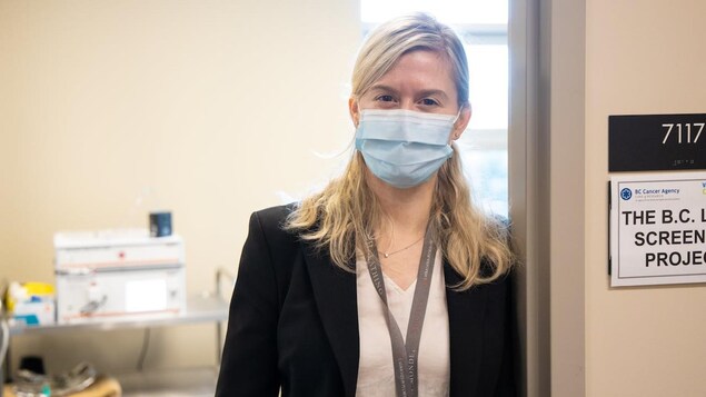 Une femme qui porte un masque médicale est appuyée dans le cadre d'une porte.