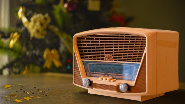 Une ancienne radio repose sur une table de bois devant un sapin de Noël.