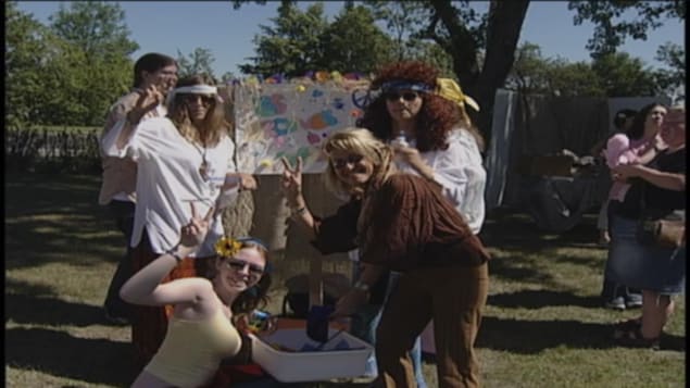 Des personnes déguisées en hippie font le signe de la paix de la main. 