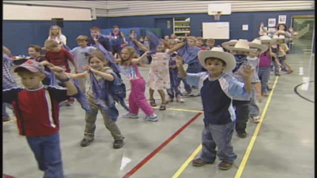 Des enfants dansent en ligne avec des chapeaux de cowboys.