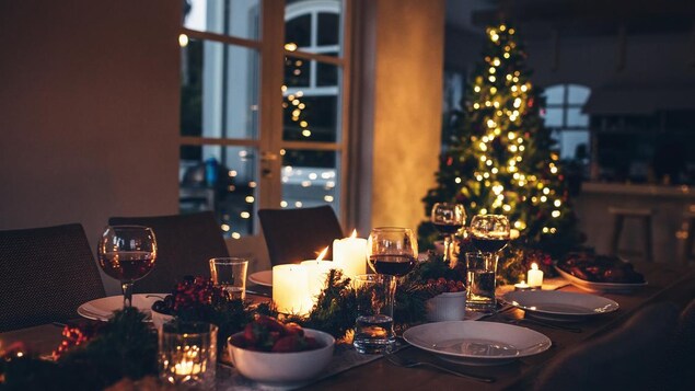 Une table est décorée de bougies, de branches de sapin et de canneberges, à côté d'un sapin de Noël illuminé