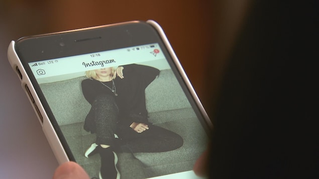 Une personne tient un cellulaire dans lequel on peut voir une photo publiée sur Instagram.