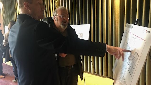 Un homme montre du doigt le plan d'un projet immobilier un tableau alors qu'un autre écoute Un homme montre du doigt le plan d'un projet immobilier un tableau alors qu'un autre écoute