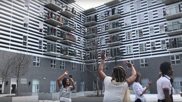 Des personnes âgées sur des balcons et de jeunes gens sur un parterre dansent au rythme de la chanson Let's Twist Again.