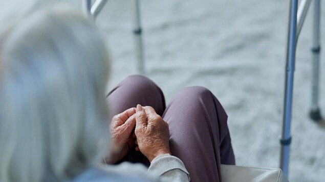 Une femme âgée assise à côté de sa marchette.