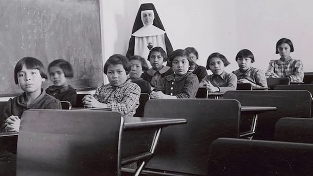 Mga batang Indigenous at isang madre sa loob ng classroom.1940 年曼尼托巴省 Cross Lake的原住民寄宿学校 Indian Residential School 。