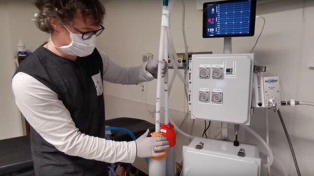 Un homme avec un masque et des gants manipule un respirateur artificiel. 