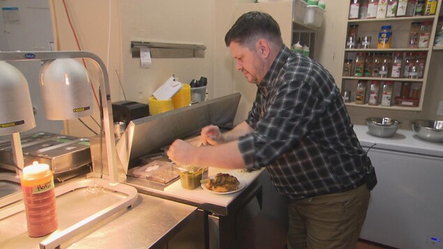 Un homme dans une cuisine industrielle prépare des ailes de poulet.