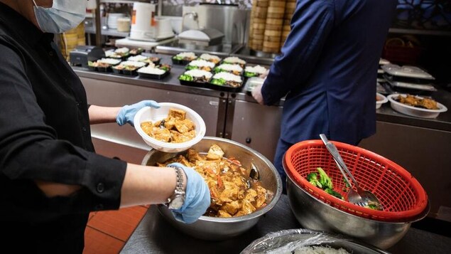 Des cuisiniers portant des masques préparent des plats pour emporter.