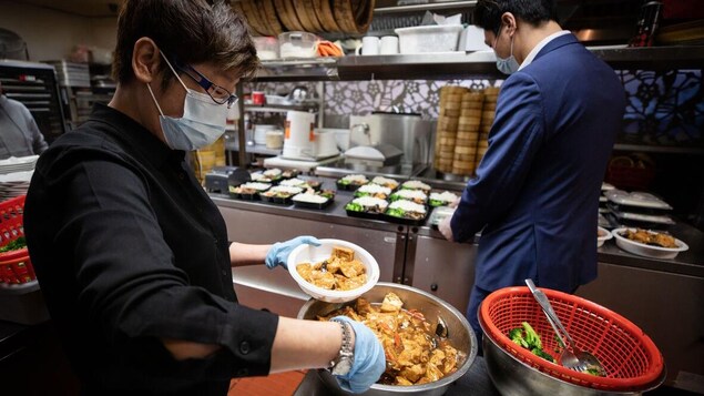 Des cuisiniers portant des masques préparent des plats pour emporter.