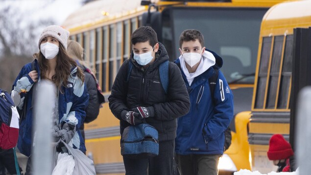 Des élèves portant un masque descendent d'un autobus scolaire.