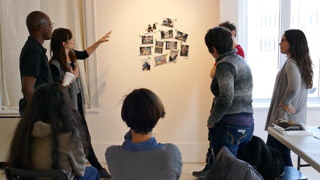 L'artiste Dominique Rey pointe et parle aux participants au sujet des photos accrochées au mur. L'artiste Dominique Rey pointe et parle aux participants au sujet des photos accrochées au mur.