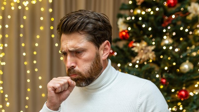 Un homme tousse devant un sapin à Noël.