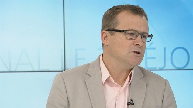 Richard Saillant porte des lunettes de vue. Un veston avec chemise. Il est en entrevue dans un studio de télévision Richard Saillant porte des lunettes de vue. Un veston avec chemise. Il est en entrevue dans un studio de télévision