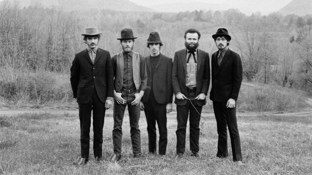 Rick Danko, Levon Helm, Richard Manuel, Garth Hudson, Robbie Robertson se tiennent côte à côte dans un champ avec des arbres en arrière-plan. Rick Danko, Levon Helm, Richard Manuel, Garth Hudson, Robbie Robertson se tiennent côte à côte dans un champ avec des arbres en arrière-plan.